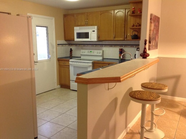 kitchen featuring decorative backsplash, kitchen peninsula, light tile patterned flooring, a breakfast bar, and white appliances