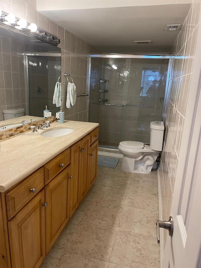 bathroom featuring walk in shower, vanity, toilet, and tile walls