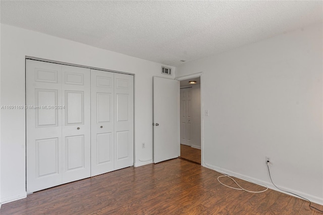 unfurnished bedroom featuring a textured ceiling, dark hardwood / wood-style floors, and a closet