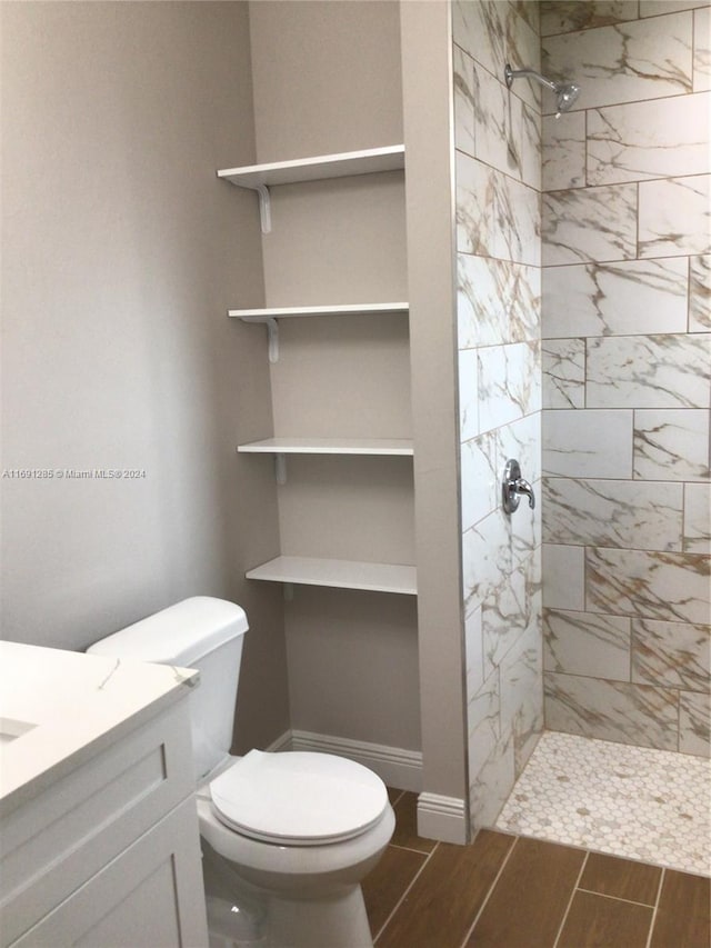 bathroom with tile patterned flooring, a tile shower, vanity, and toilet