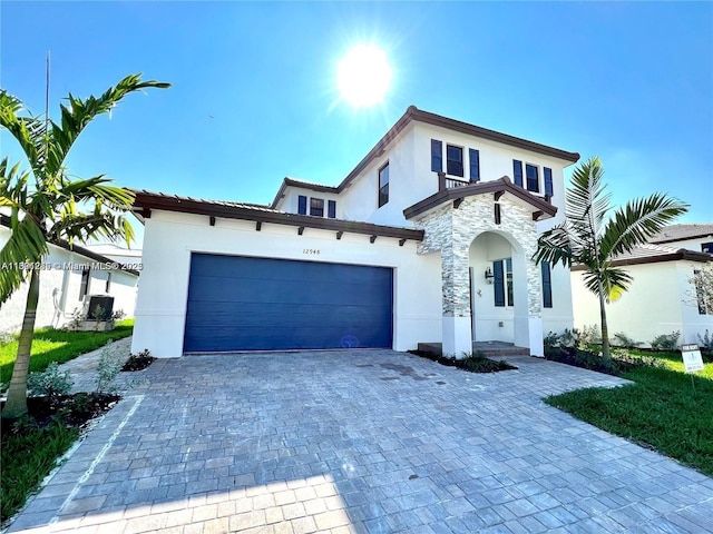 mediterranean / spanish home featuring decorative driveway, an attached garage, stone siding, and stucco siding