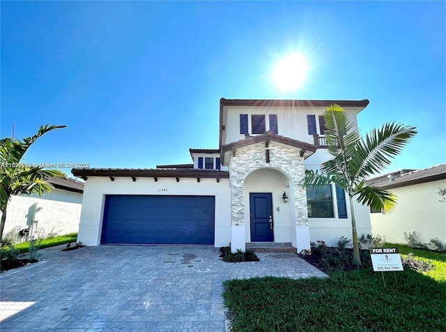 mediterranean / spanish-style home with a garage, stucco siding, decorative driveway, and stone siding