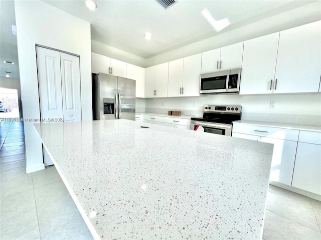 kitchen with stainless steel appliances, white cabinetry, light stone countertops, light tile patterned floors, and a center island