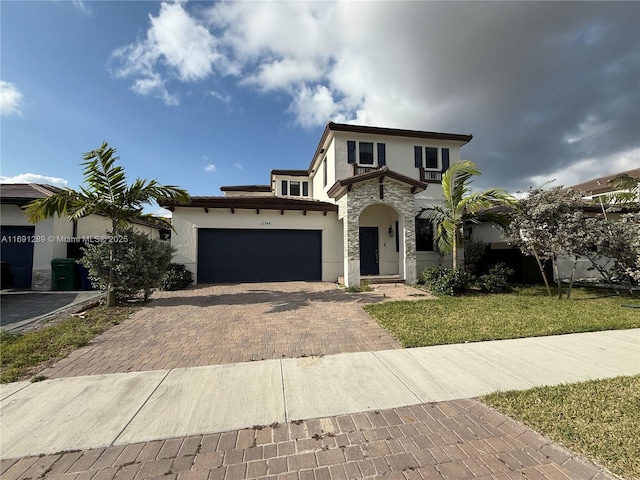 mediterranean / spanish house with an attached garage, stone siding, stucco siding, a front yard, and decorative driveway