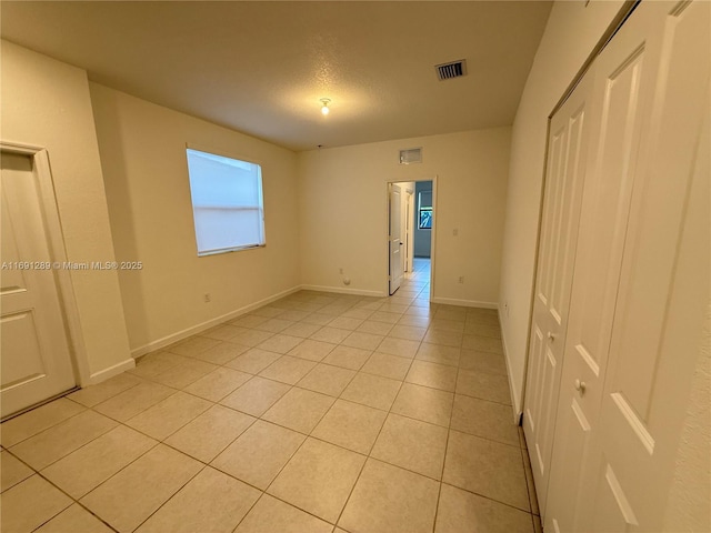 unfurnished bedroom featuring light tile patterned flooring, baseboards, visible vents, and a closet