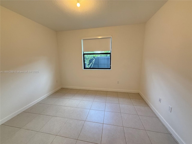 empty room with a textured ceiling, baseboards, and light tile patterned floors