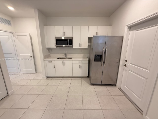 kitchen with white cabinets, appliances with stainless steel finishes, a sink, light countertops, and visible vents