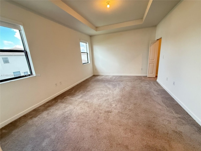 carpeted spare room featuring baseboards and a tray ceiling