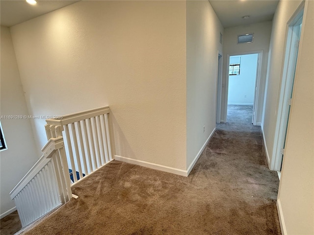 corridor with carpet floors, visible vents, baseboards, and an upstairs landing
