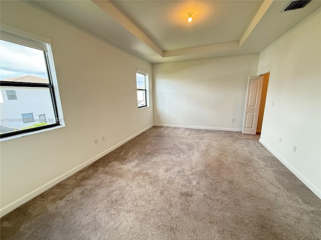 carpeted spare room with a tray ceiling, visible vents, and baseboards