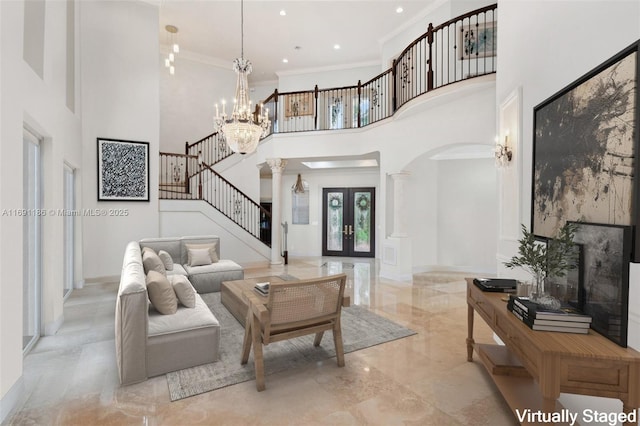 living room with a towering ceiling, decorative columns, ornamental molding, a notable chandelier, and french doors