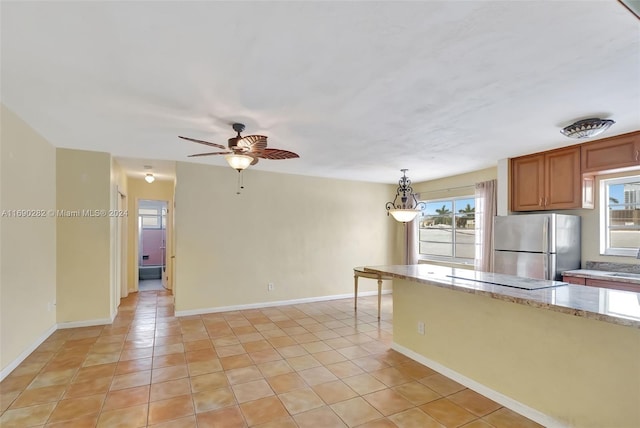 kitchen with a wealth of natural light, decorative light fixtures, stainless steel refrigerator, and light tile patterned floors