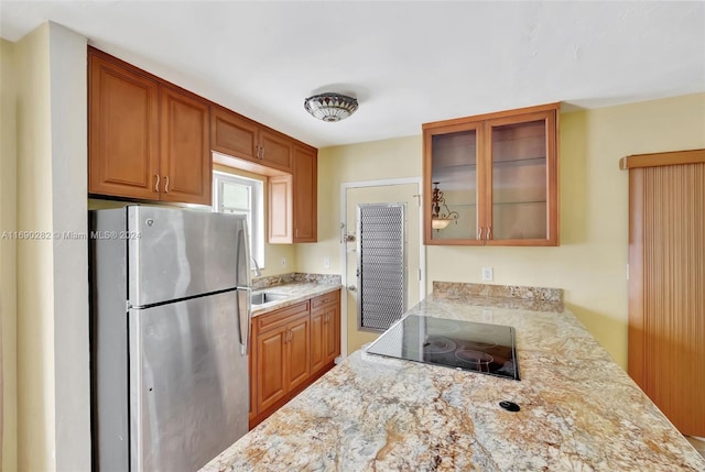 kitchen featuring black electric cooktop, light stone counters, and stainless steel fridge