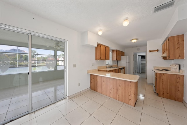 kitchen featuring light tile patterned flooring, white appliances, kitchen peninsula, a water view, and a textured ceiling