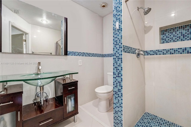 bathroom featuring sink, a tile shower, tile patterned floors, toilet, and tile walls