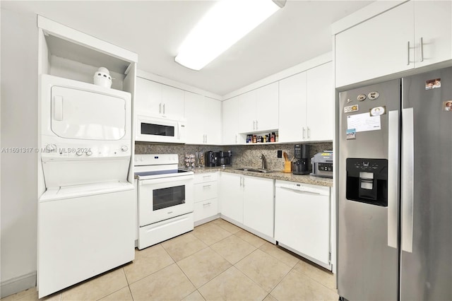 kitchen featuring white cabinets, sink, backsplash, stacked washer and dryer, and white appliances