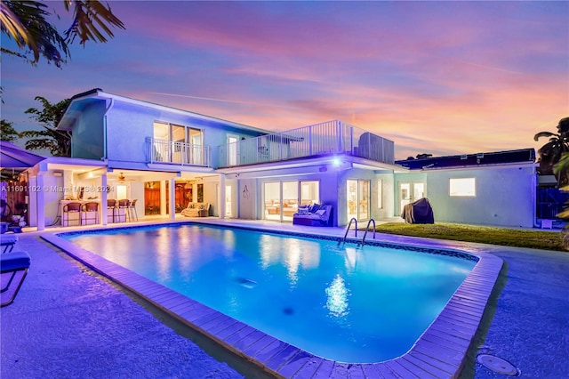 pool at dusk featuring exterior bar and a patio