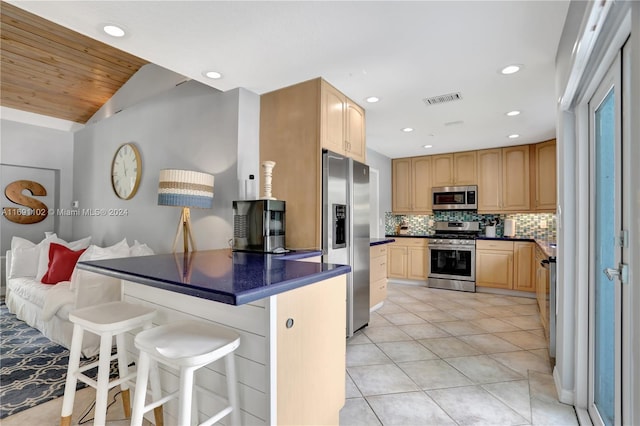 kitchen with tasteful backsplash, lofted ceiling, a breakfast bar area, light tile patterned flooring, and appliances with stainless steel finishes