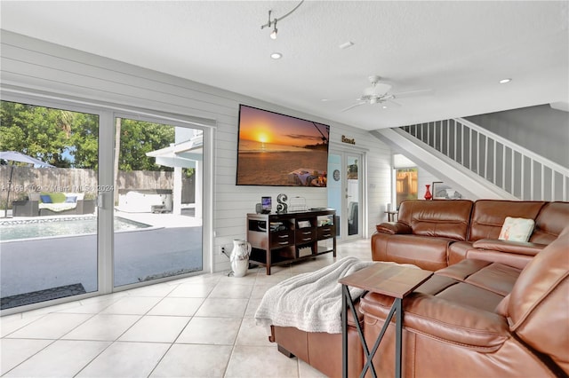 living room featuring ceiling fan, wood walls, light tile patterned flooring, and a textured ceiling