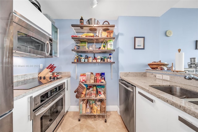 kitchen featuring white cabinetry, stainless steel appliances, sink, light stone counters, and light tile patterned floors