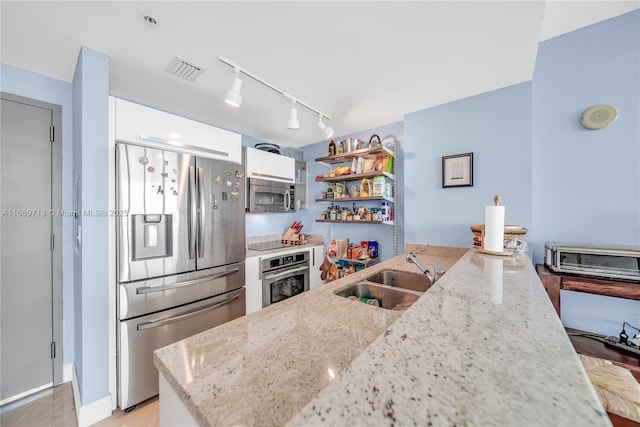 kitchen with appliances with stainless steel finishes, sink, rail lighting, white cabinets, and light stone countertops