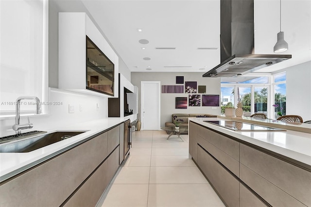 kitchen with island range hood, black electric stovetop, decorative light fixtures, light tile patterned floors, and sink