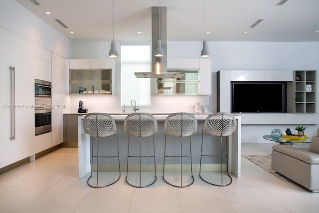 kitchen with white cabinets, a kitchen bar, island range hood, and decorative light fixtures