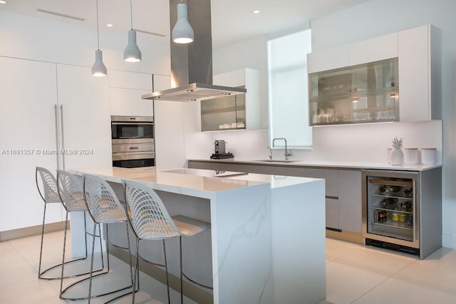 kitchen with island range hood, wine cooler, white cabinetry, decorative light fixtures, and sink