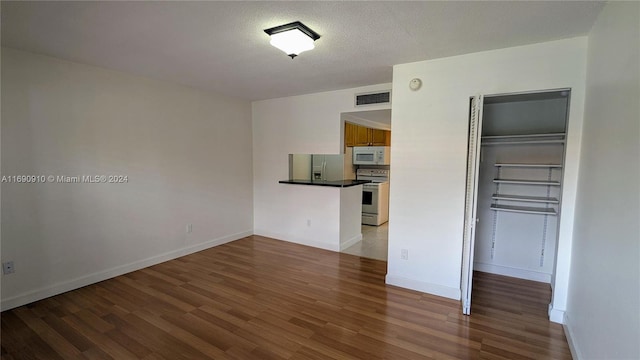 unfurnished bedroom with a textured ceiling, wood-type flooring, stainless steel refrigerator with ice dispenser, and a closet