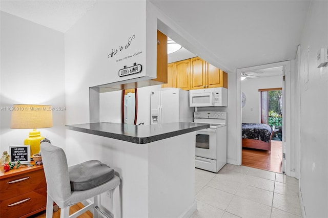 kitchen with a breakfast bar, white appliances, ceiling fan, light tile patterned floors, and kitchen peninsula