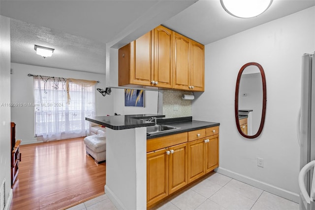 kitchen with kitchen peninsula, stainless steel fridge, a textured ceiling, sink, and light tile patterned flooring