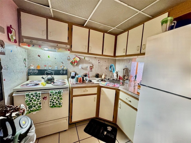 kitchen featuring under cabinet range hood, a drop ceiling, backsplash, white appliances, and light countertops