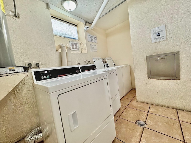 shared laundry area with washing machine and clothes dryer, light tile patterned floors, and a textured wall