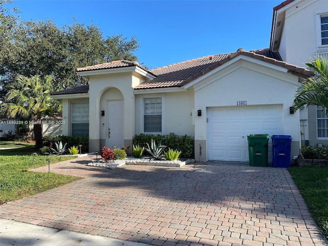 mediterranean / spanish-style home featuring stucco siding, an attached garage, a tile roof, and decorative driveway