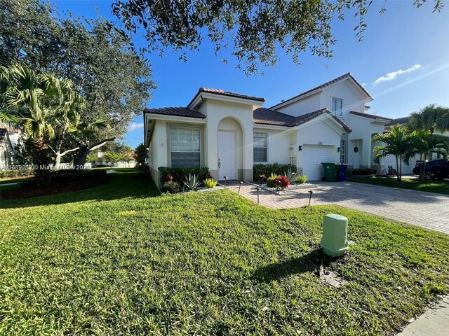 mediterranean / spanish-style home with a front yard, stucco siding, a garage, a tile roof, and decorative driveway