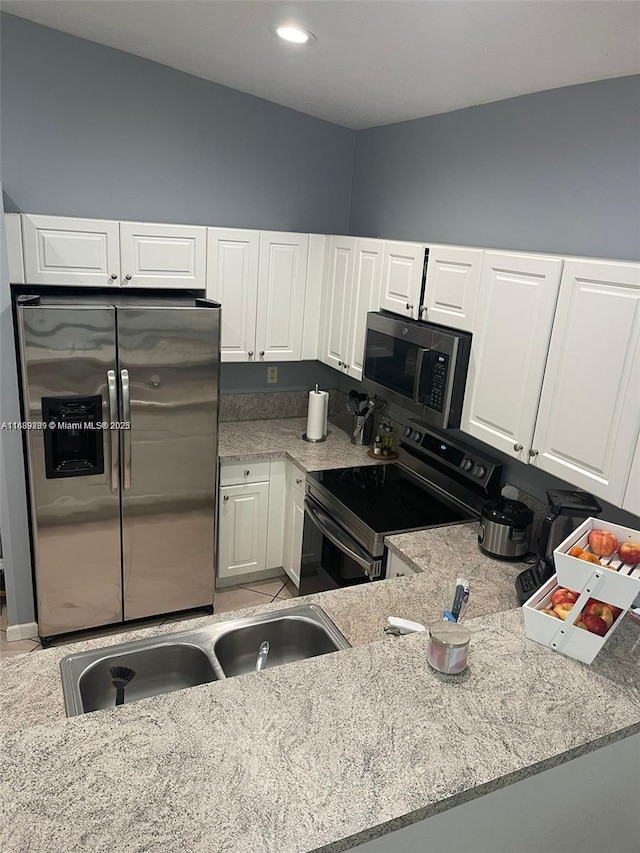 kitchen featuring light stone counters, white cabinets, appliances with stainless steel finishes, and a sink