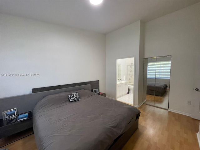 bedroom featuring a towering ceiling, a closet, light wood-type flooring, and ensuite bathroom