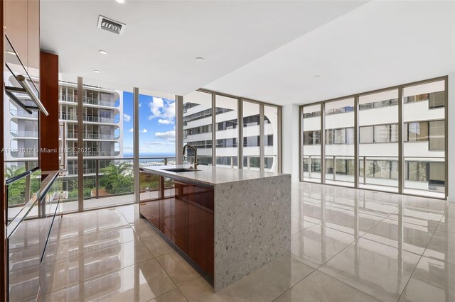 kitchen with light stone countertops, light tile patterned flooring, a center island with sink, and floor to ceiling windows