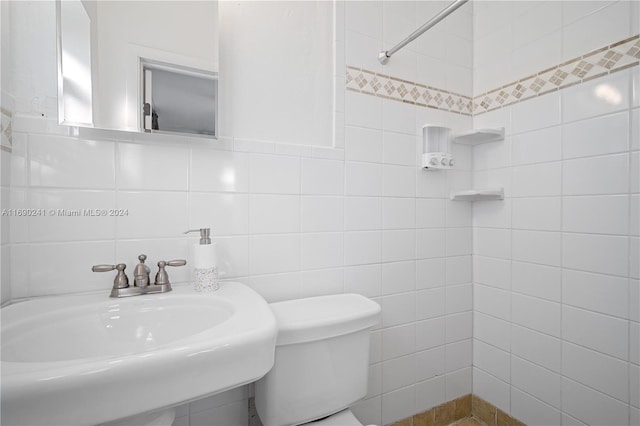 bathroom featuring toilet, tile walls, and sink