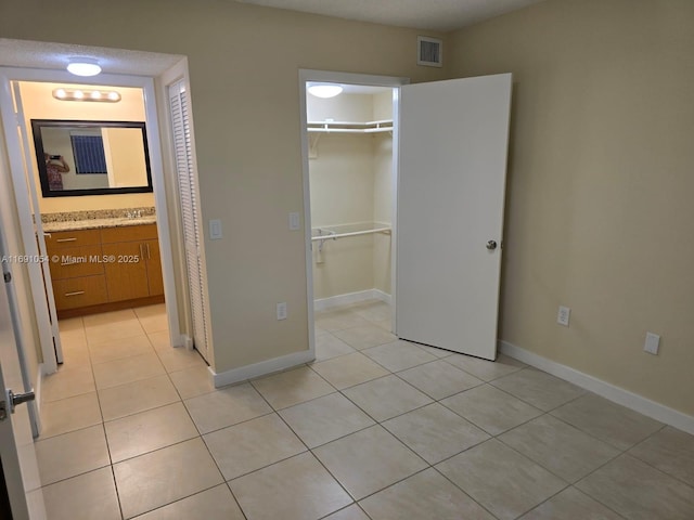 unfurnished bedroom with ensuite bath, a walk in closet, a closet, and light tile patterned flooring