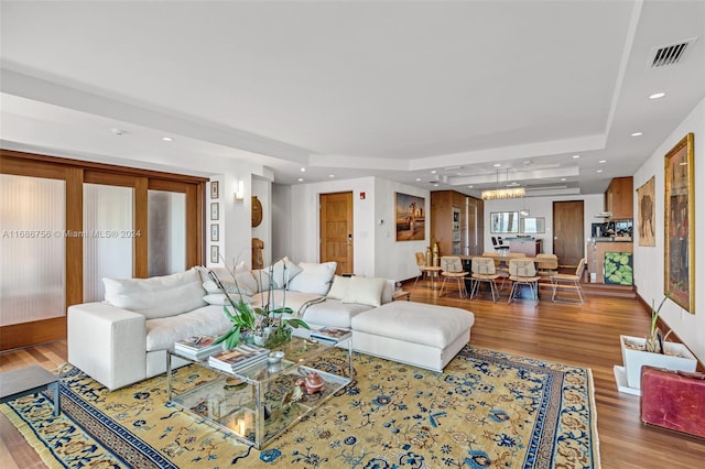 living room with hardwood / wood-style flooring, a tray ceiling, and a notable chandelier