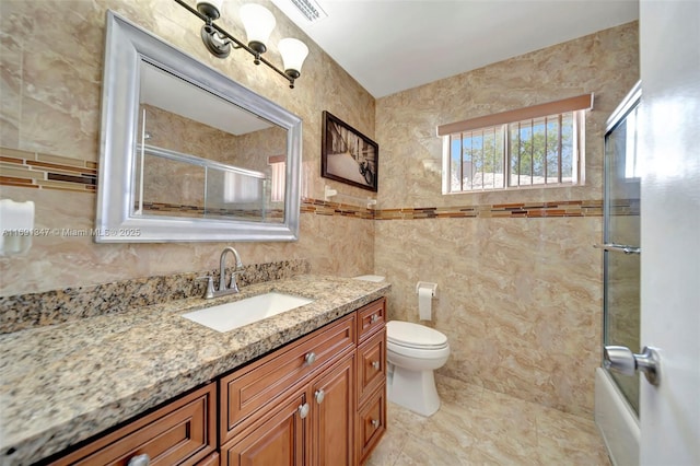 full bathroom featuring vanity, toilet, bath / shower combo with glass door, and tile walls