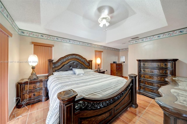 tiled bedroom featuring ceiling fan, a textured ceiling, and a tray ceiling