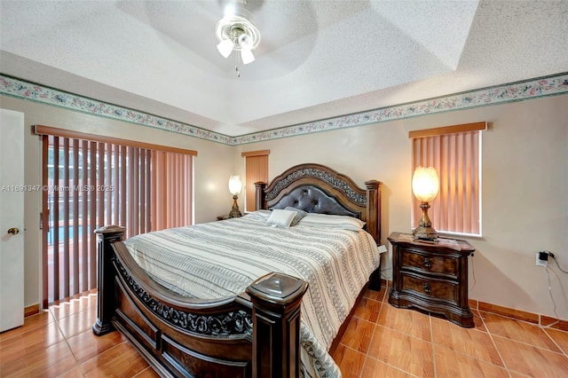 bedroom with ceiling fan, tile patterned floors, a textured ceiling, and a tray ceiling