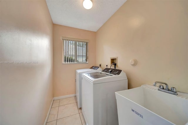 clothes washing area featuring washer and dryer, sink, a textured ceiling, and light tile patterned floors