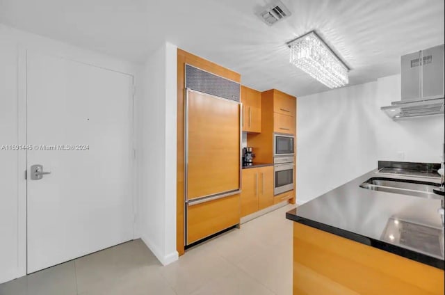 kitchen featuring light tile patterned flooring, range hood, built in appliances, light brown cabinets, and sink