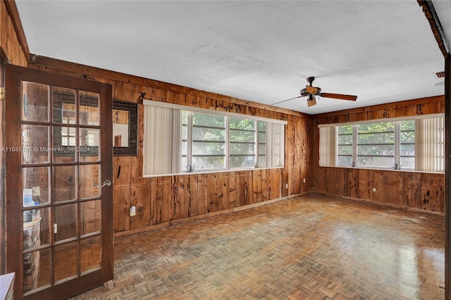 unfurnished room with parquet floors, wooden walls, and ceiling fan