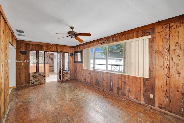 empty room featuring dark parquet floors, wooden walls, a textured ceiling, and ceiling fan