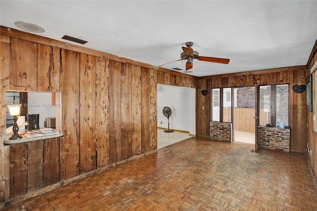 unfurnished living room featuring ceiling fan, wooden walls, and parquet floors