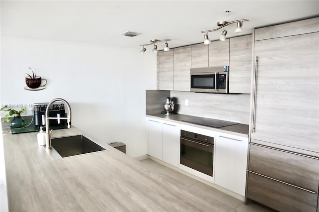 kitchen with decorative backsplash, appliances with stainless steel finishes, light wood-type flooring, sink, and white cabinets